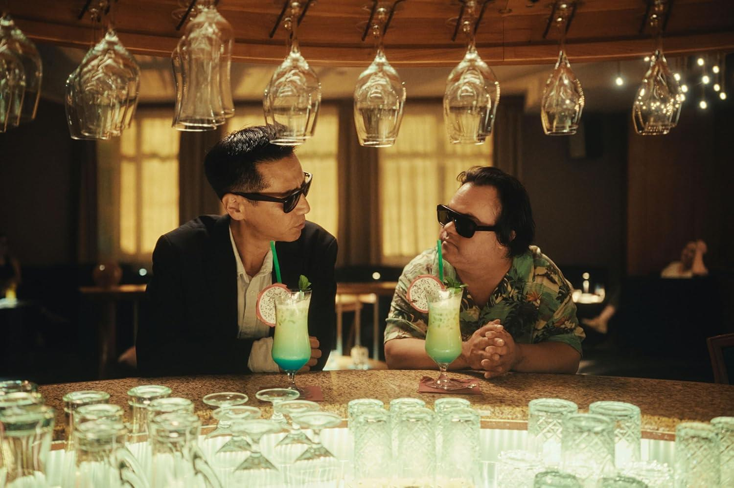 Zwei Männer mit Sonnenbrillen sitzen an einer Bar und trinken grüne Cocktails mit Drachenfrucht.