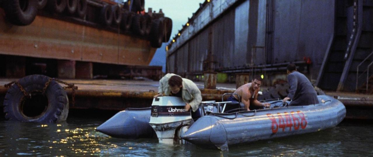 Männer in einem Schlauchboot mit Außenbordmotor vor einem großen Schiff und Kai.