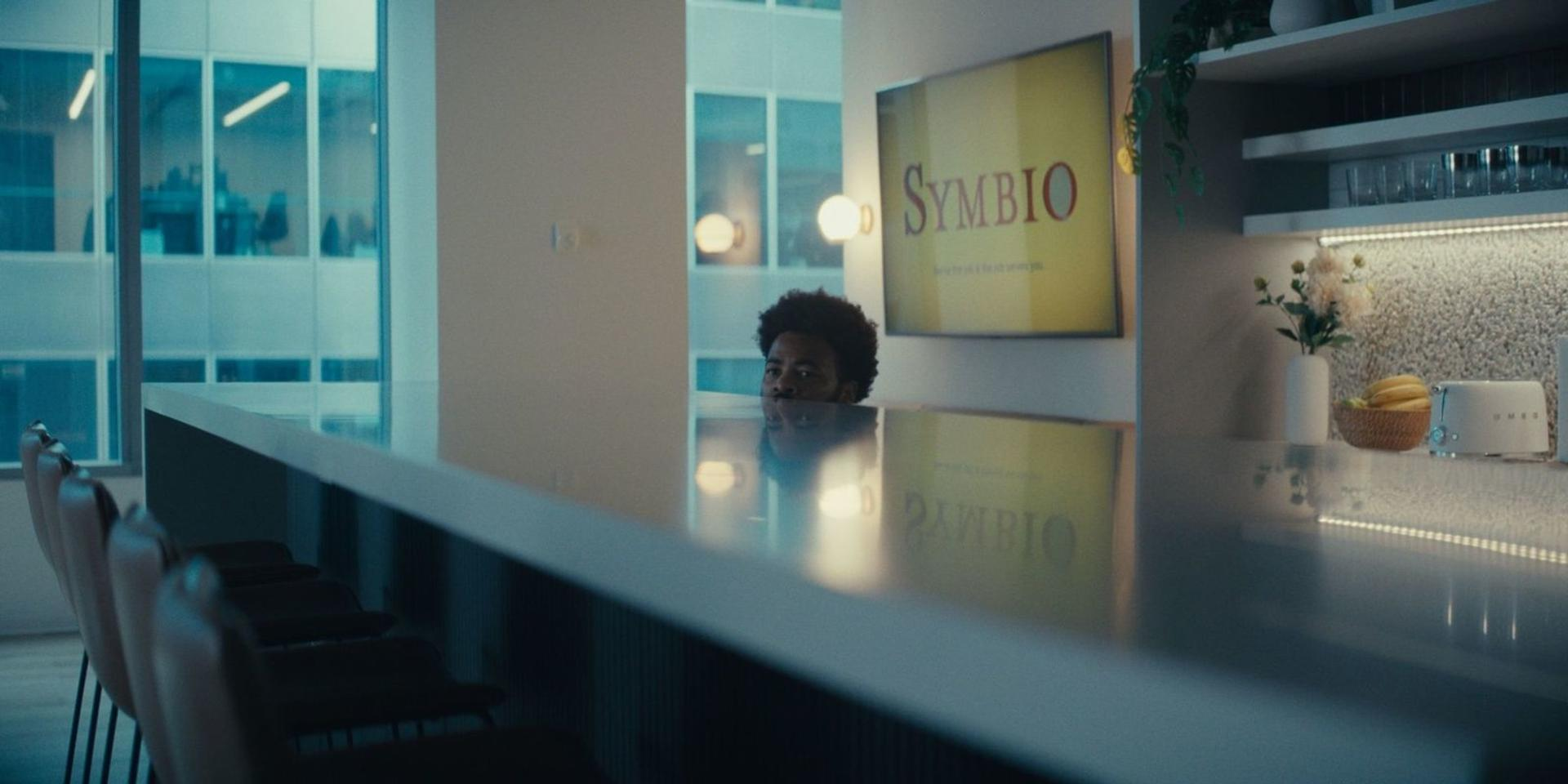 Mann lugt über eine glänzende Theke in einem modernen Büro-Pausenraum mit Symbio-Logo.
