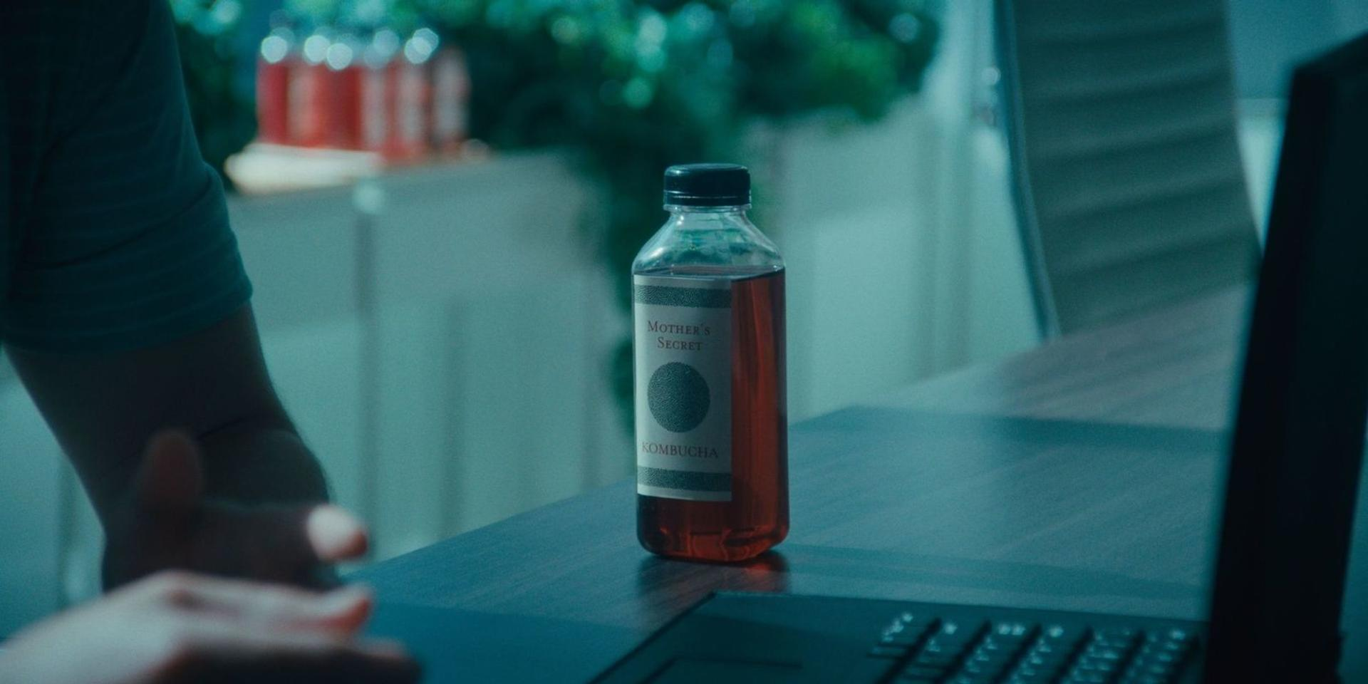 Eine Flasche "Mother's Secret" Kombucha steht auf einem Tisch neben einem Laptop.