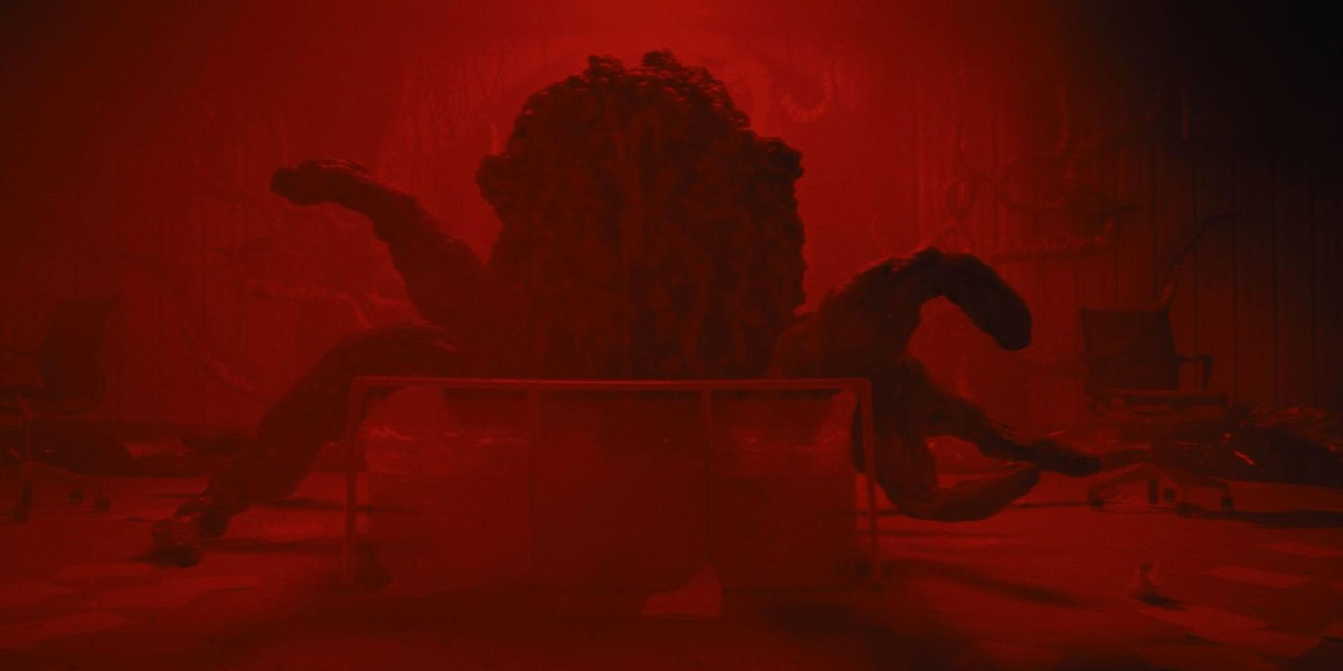 Ein rotes, schleimiges Monster mit Tentakeln ragt über einen Glastisch.