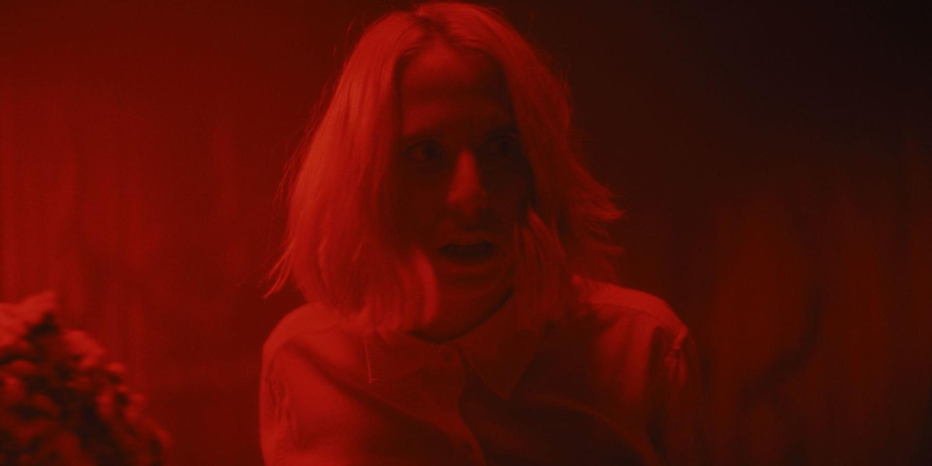 Eine Frau mit hellblonden Haaren blickt erschrocken in rotes Licht.