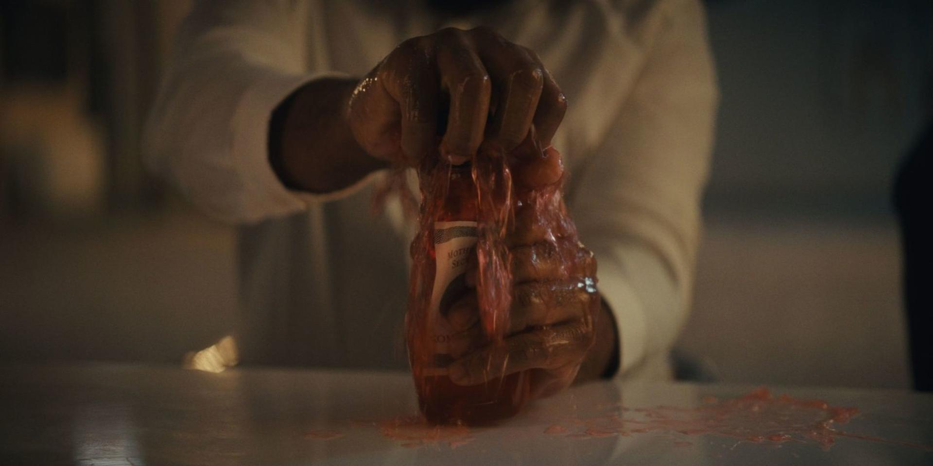 Eine Hand drückt eine Flasche mit roter Flüssigkeit aus, wodurch sie herausläuft.