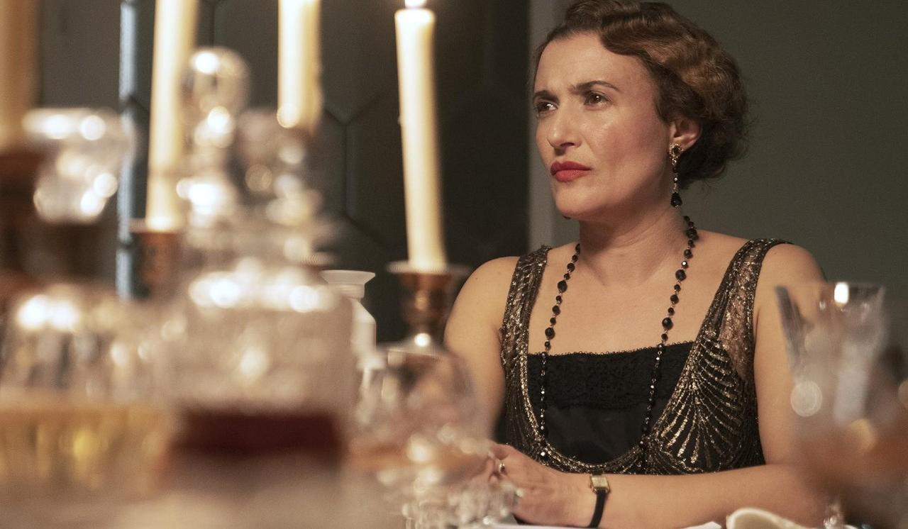Frau in einem schwarzen Kleid mit Goldmuster sitzt an einem Tisch mit Kerzen.