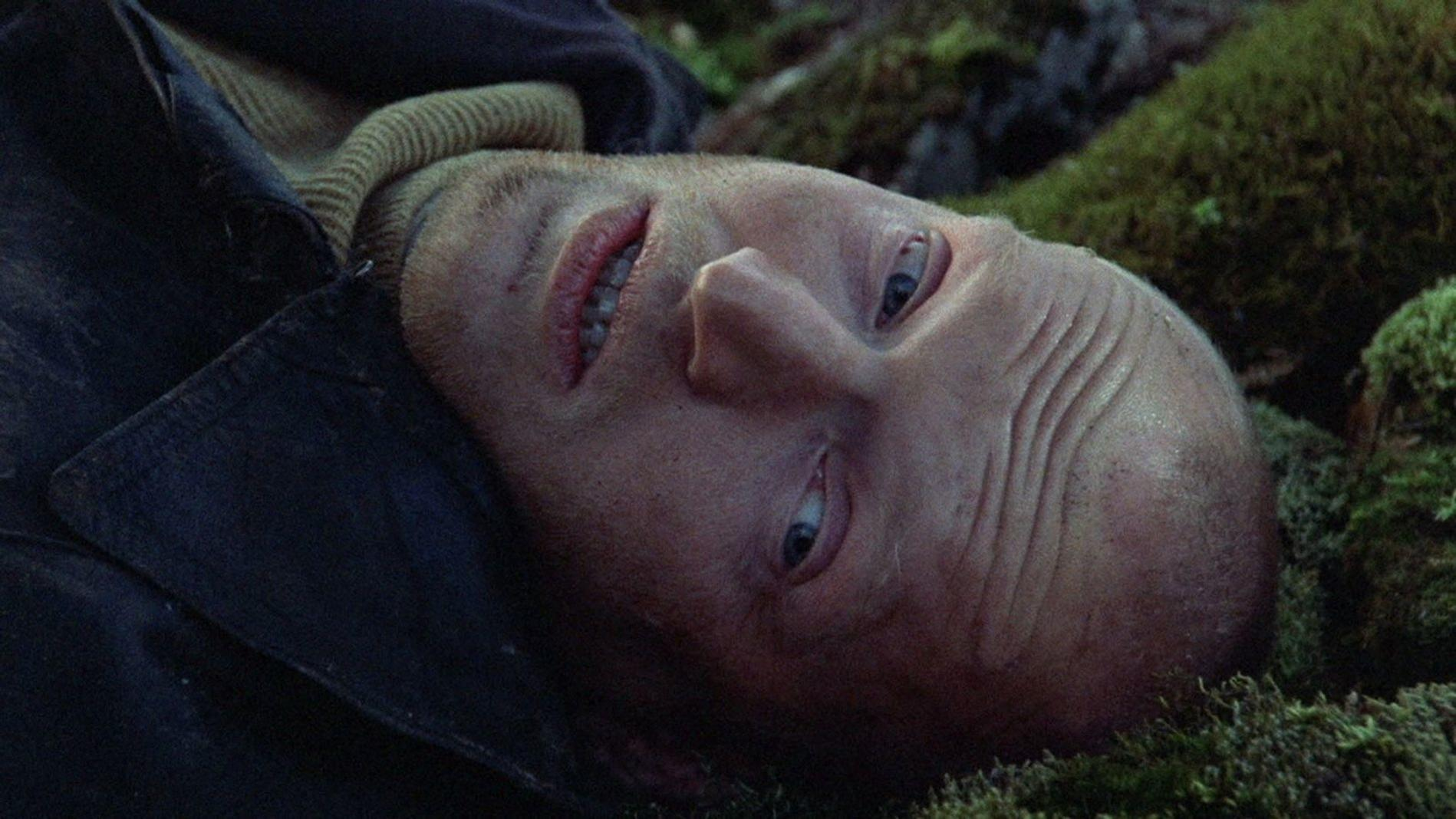 Nahaufnahme eines Mannes, der auf moosigem Boden liegt und mit blauen Augen nach oben blickt.