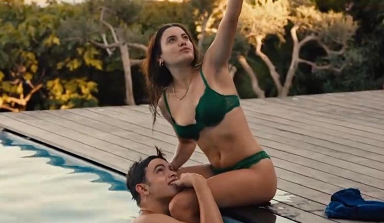 Ein Mann und eine Frau in Badekleidung sitzen auf einem Pooldeck mit Bäumen im Hintergrund.