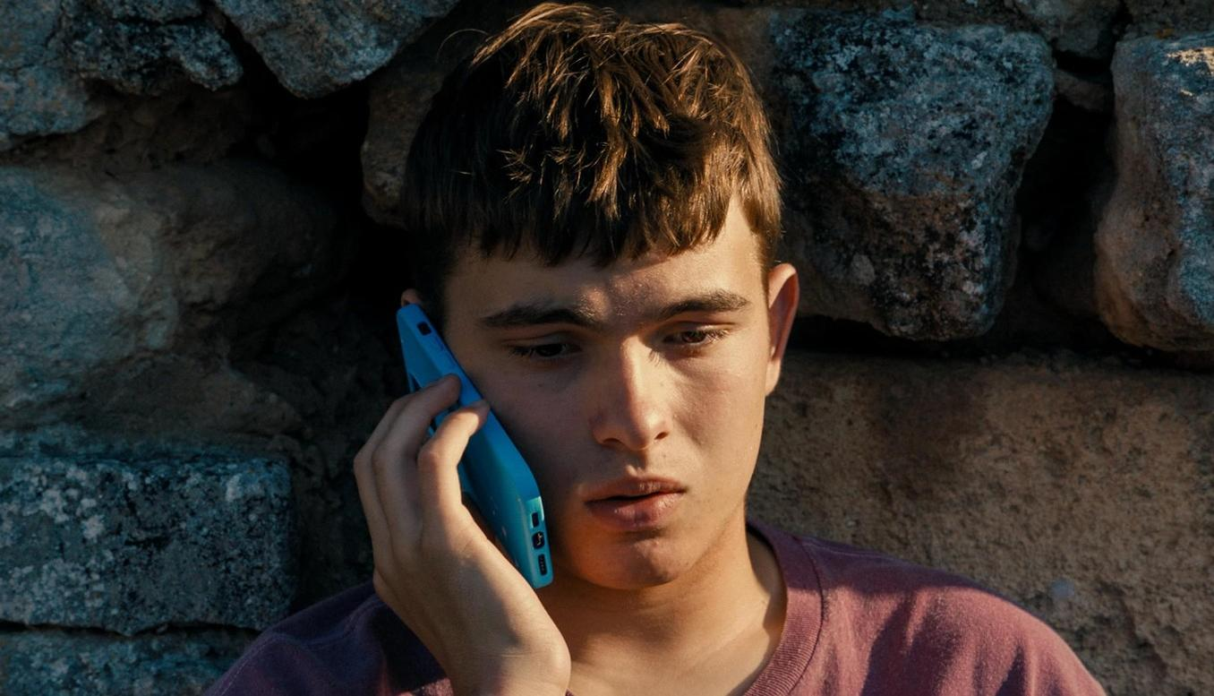 Ein Junge mit braunen Haaren telefoniert mit einem blauen Handy.