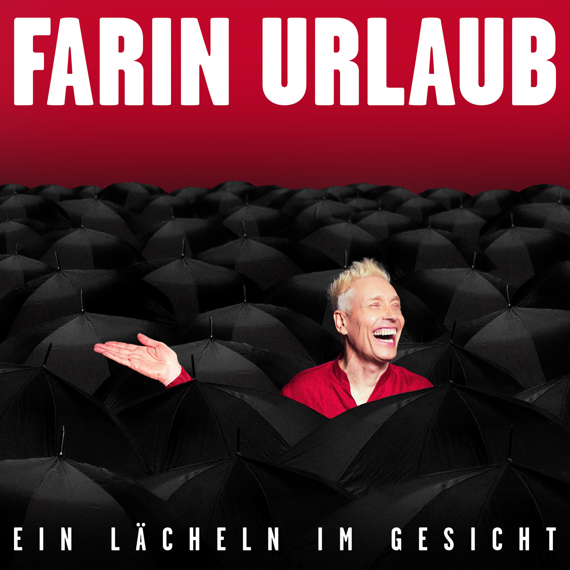 Ein Mann mit blonden Haaren in einem roten Hemd steht zwischen vielen schwarzen Regenschirmen.