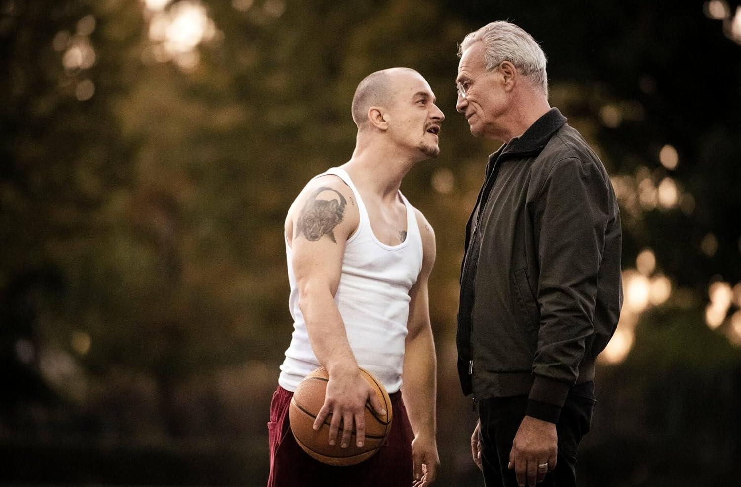 Zwei Männer stehen sich gegenüber. Einer hält einen Basketball. Hintergrund ist unscharf.