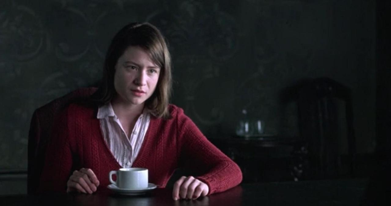 Eine Frau in einem roten Cardigan sitzt an einem Tisch mit einer Tasse Kaffee.