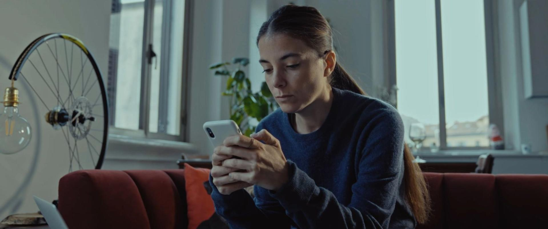 Frau mit Handy auf einem Sofa, Fahrradradlampe im Hintergrund.
