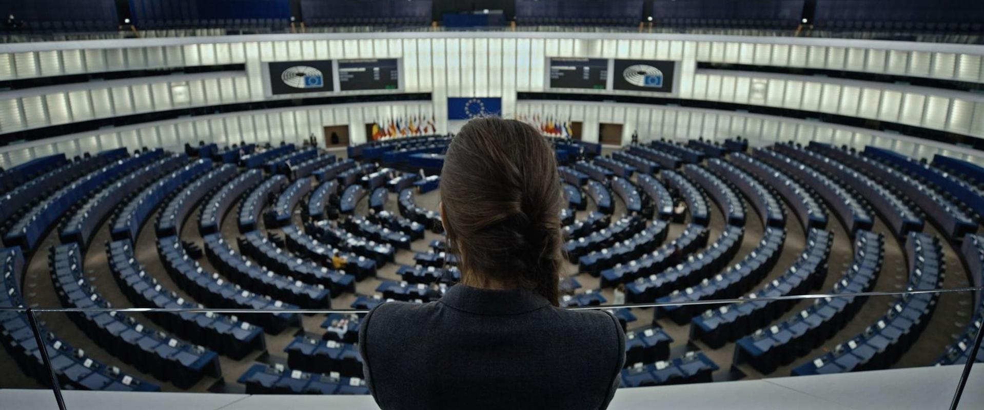 Frau blickt auf leere Sitze im Parlament. Blaue Sitze sind in Reihen angeordnet.
