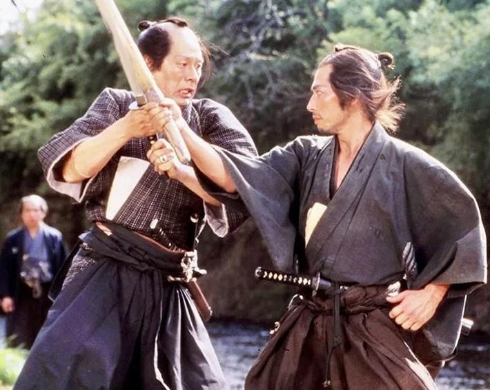 Zwei Samurai in traditioneller Kleidung kämpfen mit Schwertern in der Nähe eines Flusses.