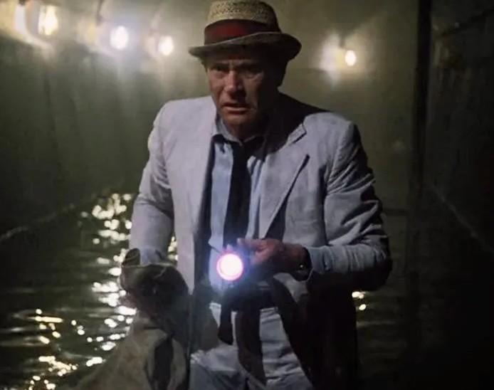 Ein Mann mit Hut und Jacke leuchtet mit einer Taschenlampe in einem dunklen, überfluteten Gang.