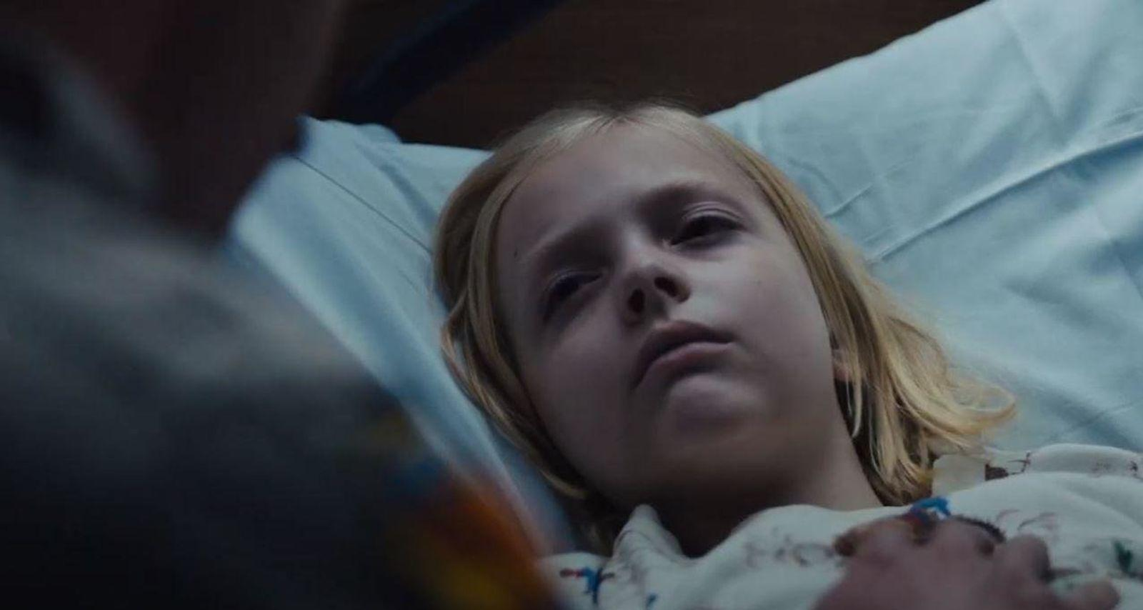 Ein junges Mädchen mit blonden Haaren liegt in einem Krankenhausbett auf einem hellblauen Laken.
