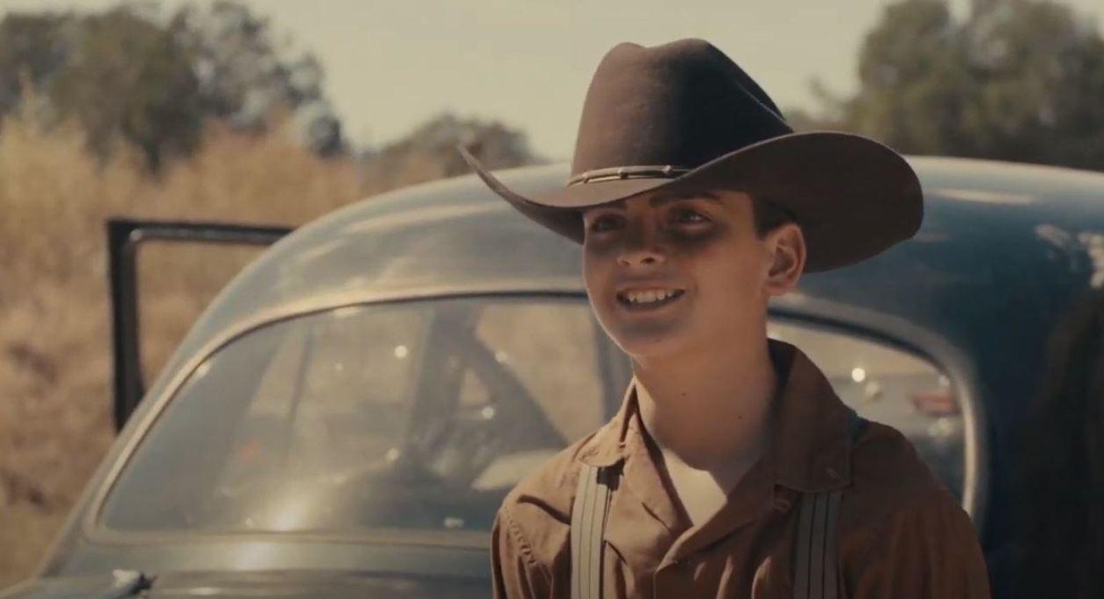 Ein Junge mit Cowboyhut steht neben einem alten Auto.