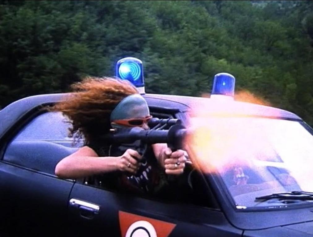 Eine Person schießt mit einer Waffe aus einem Auto mit Blaulichtern.