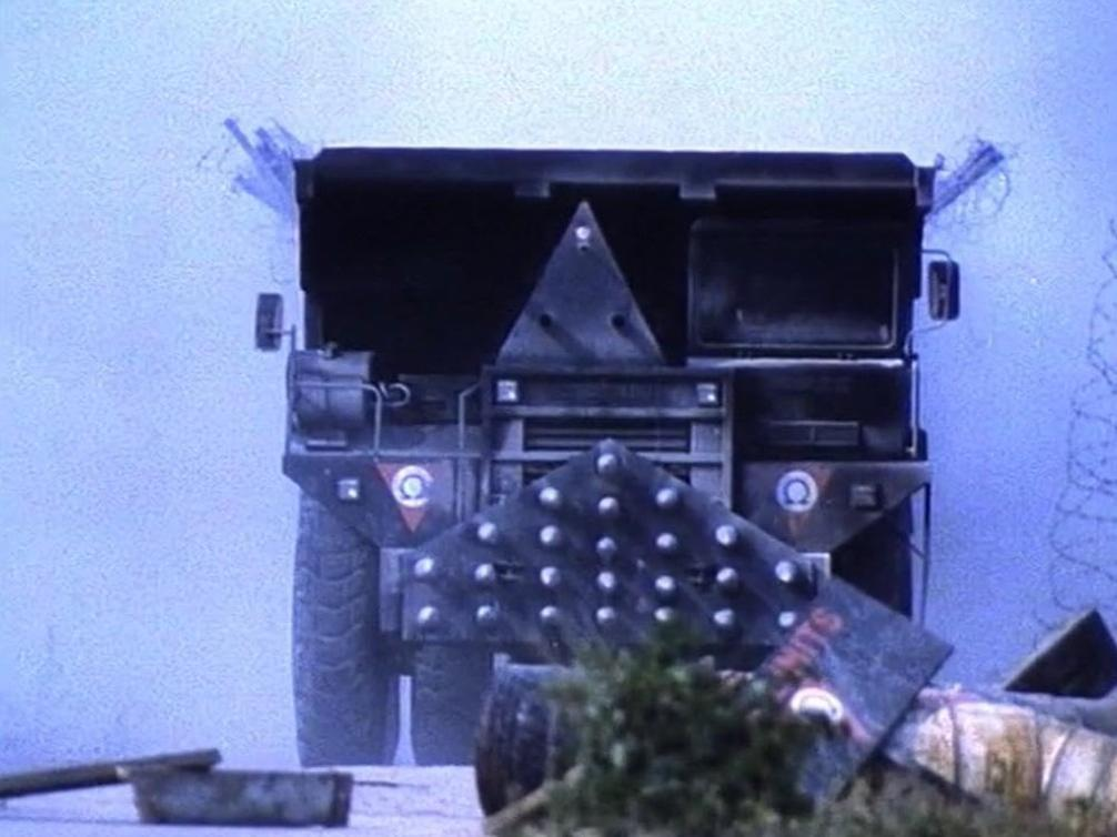 Ein schwer gepanzerter LKW mit Metallplatten und Stacheldraht im Nebel.