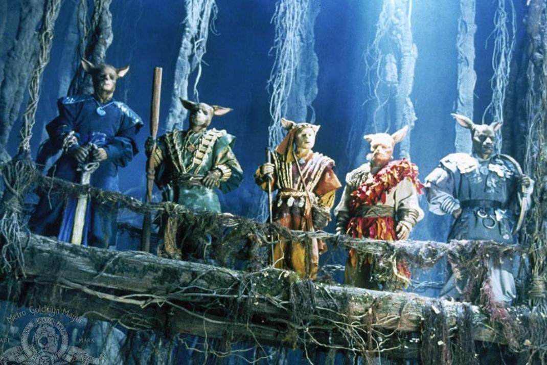 Fünf anthropomorphe Wesen mit Fellen und Ohren stehen auf einer Holzplattform.