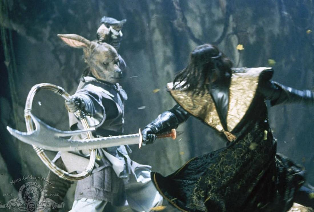 Ein Mann mit Tiermaske und Waffe kämpft gegen einen Mann in schwarzer Kleidung.