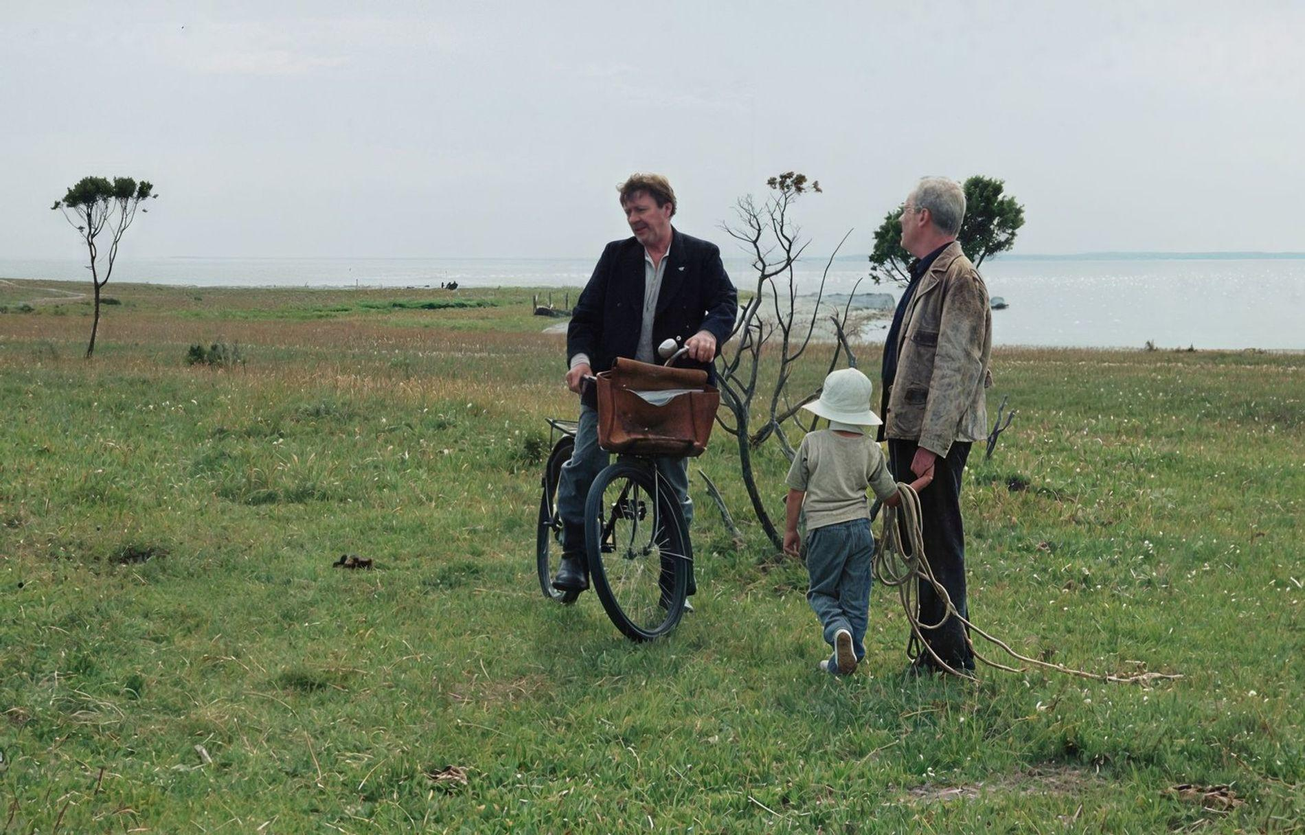 Mann auf Fahrrad spricht mit Mann und Kind am Meer.
