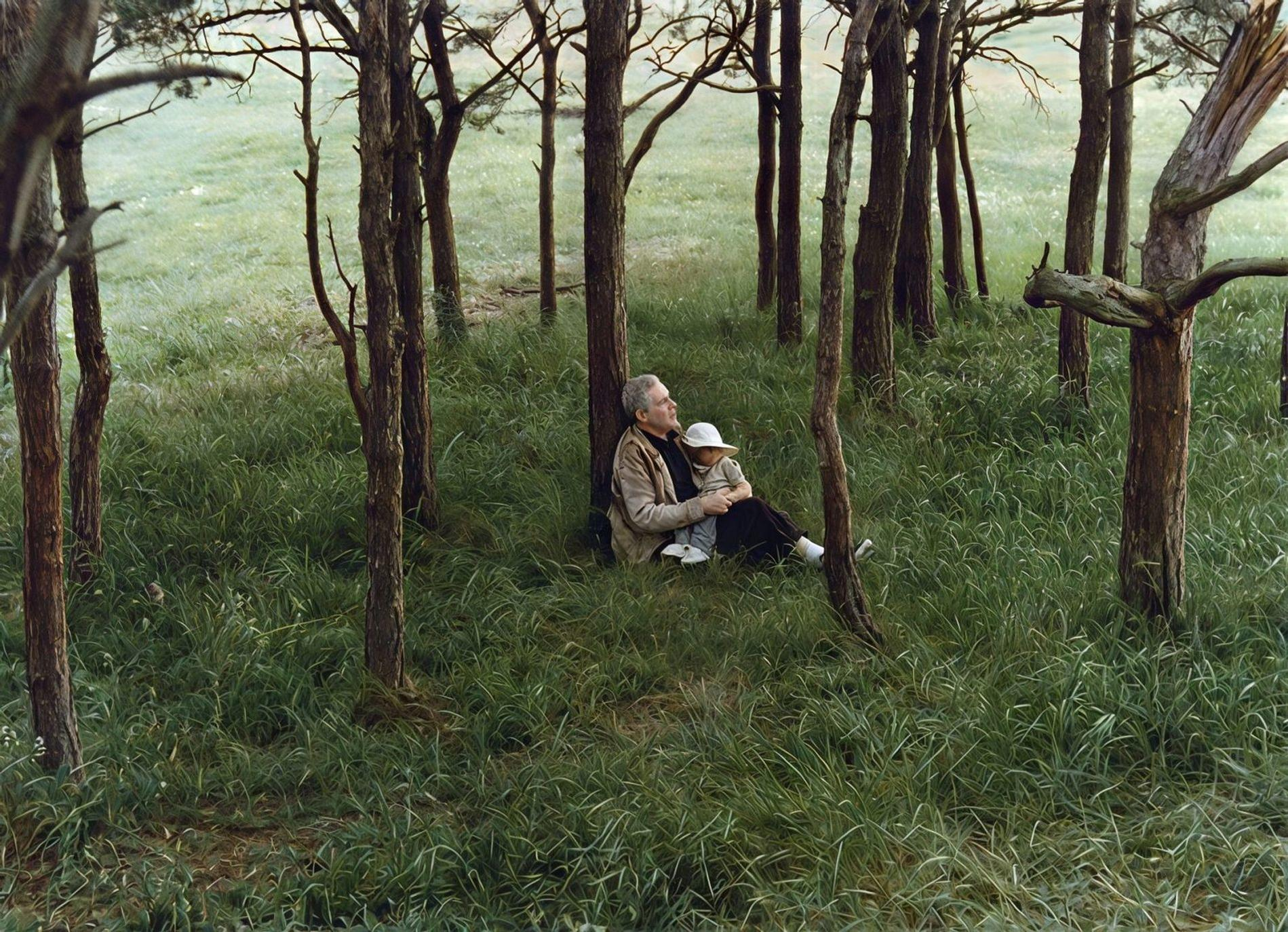 Ein Mann und ein Kind sitzen im Gras zwischen Bäumen, umarmt.