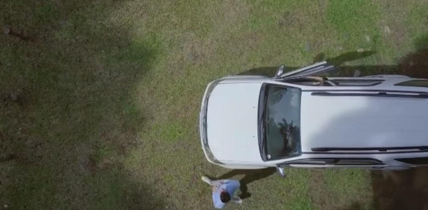 Ein Mann steht neben einem weißen Auto auf einer Grasfläche.