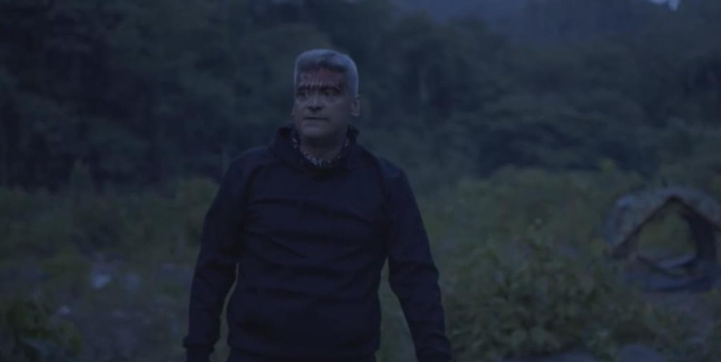 Ein Mann mit grauen Haaren und blutigem Gesicht steht im Freien.