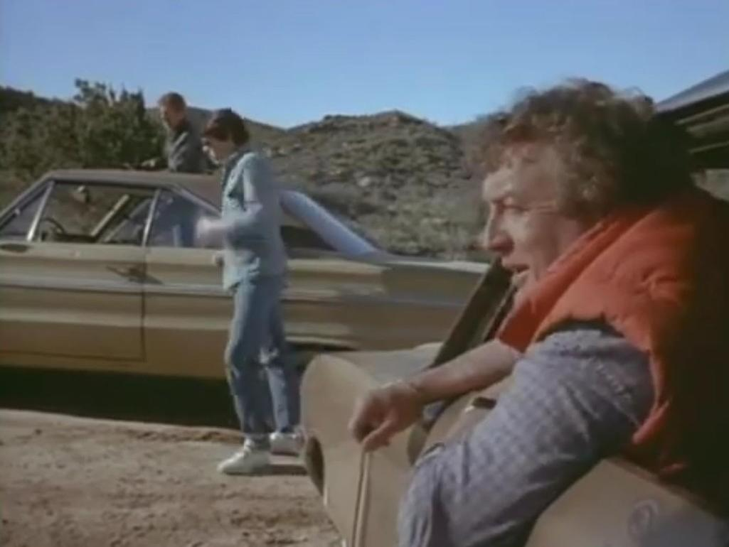 Zwei Männer und ein gelbes Auto in einer bergigen Landschaft.