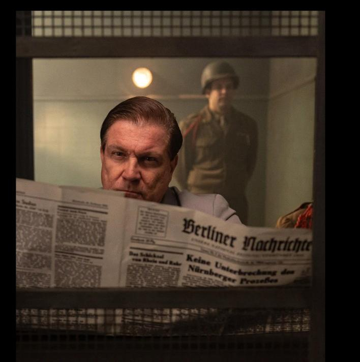 Ein Mann liest Zeitung, ein Soldat steht im Hintergrund.