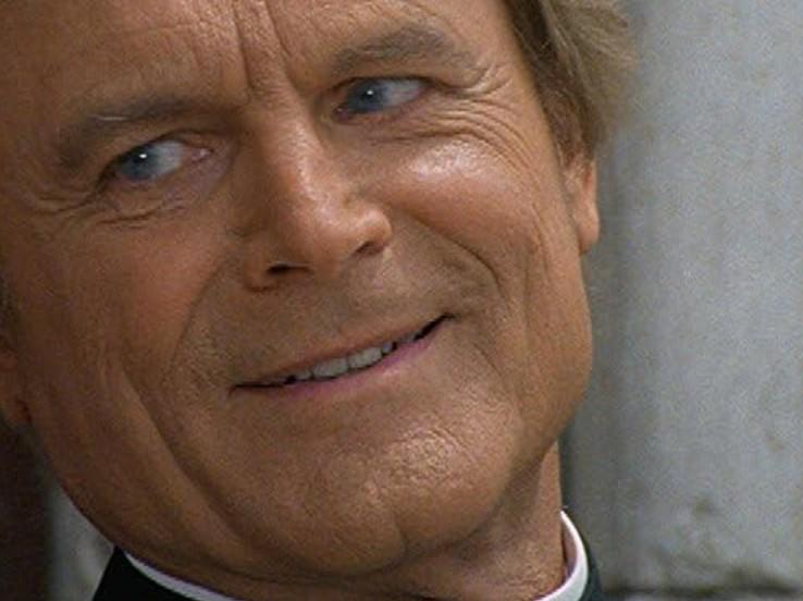 Ein älterer Mann mit blauen Augen lächelt leicht, sein Gesicht ist nah.