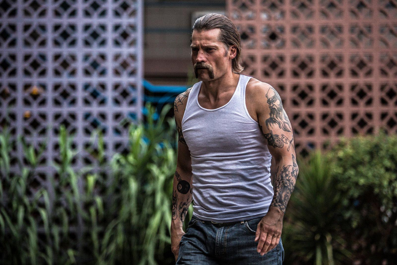 Mann mit Tanktop und Jeans geht mit Tattoos und Schnurrbart.