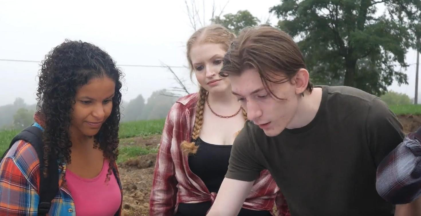 Drei junge Leute stehen draußen auf einem Feld und schauen auf etwas.