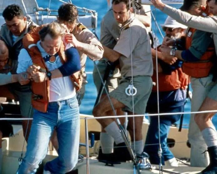 Männer in Bootshosen und Hemden helfen einem Mann mit Schwimmweste auf einem Boot.