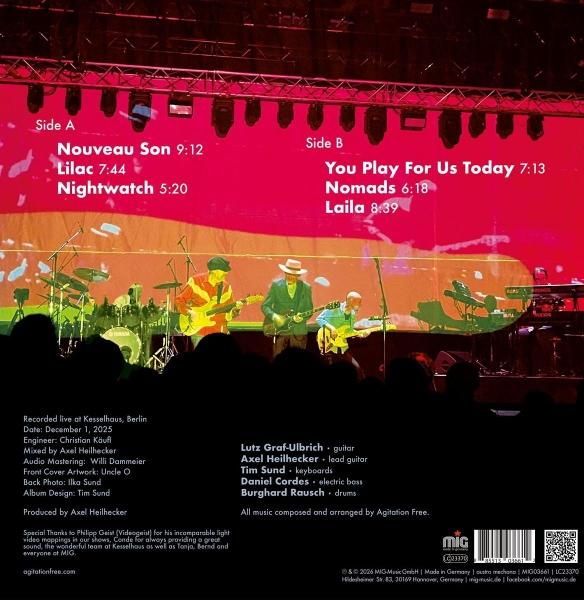 Band spielt auf einer Bühne vor rotem Hintergrund mit Liedtiteln. Silhouette des Publikums.