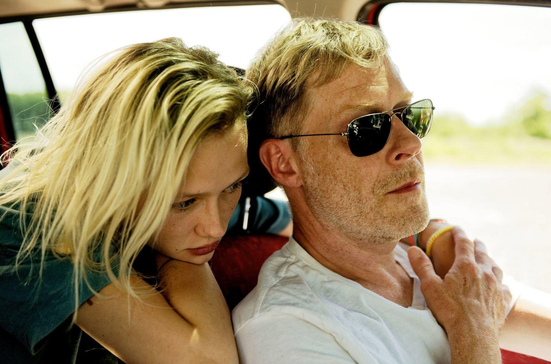 Mann mit Sonnenbrille und Frau mit blonden Haaren sitzen im Auto.