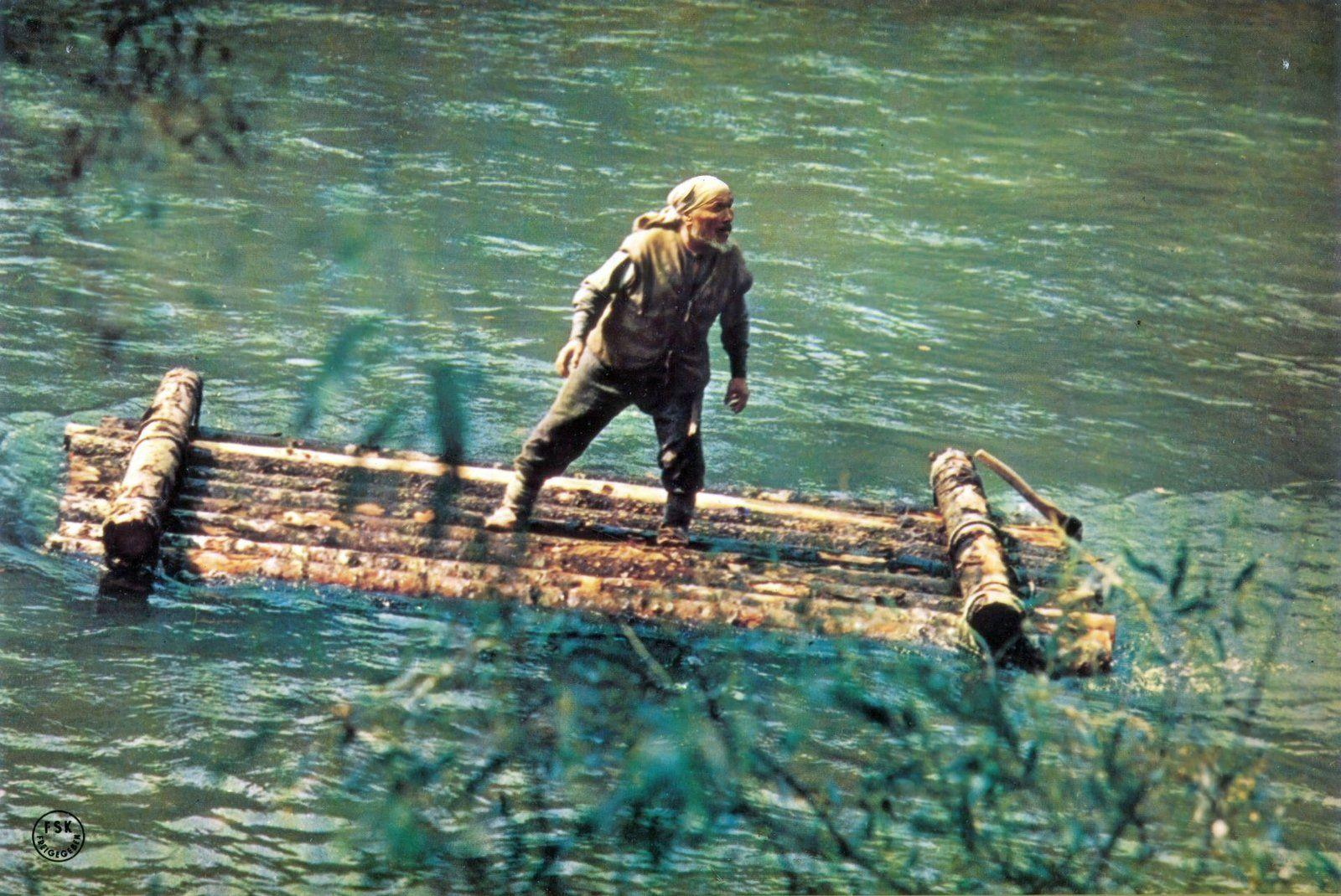 Ein Mann auf einem Holzfloß navigiert auf einem Fluss.
