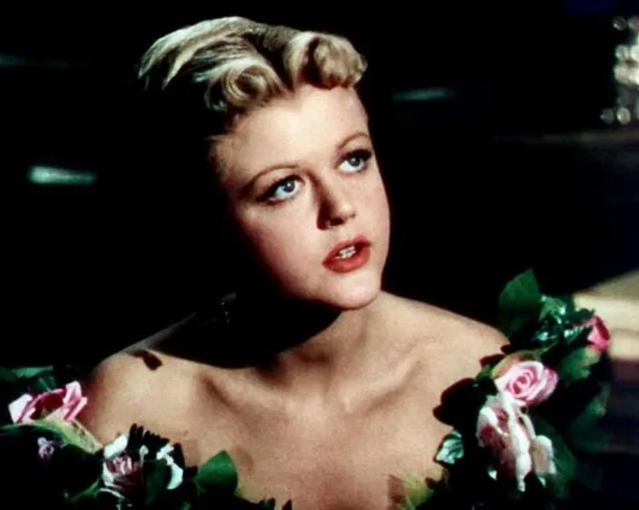 Blonde Frau mit lockigem Haar, trägt ein Kleid aus rosa Rosen und grünen Blättern.