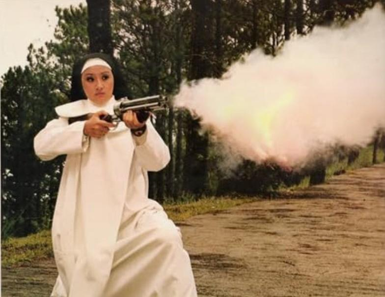 Eine Nonne in weißer Robe kniet und feuert eine Waffe ab, Rauch steigt auf.