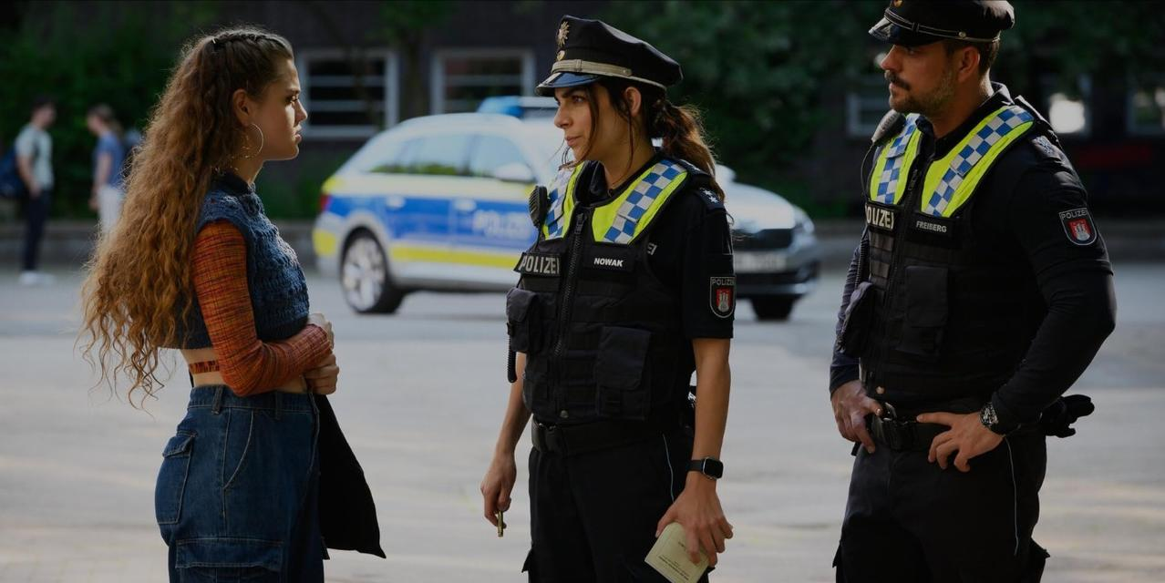 Polizisten stehen neben einer jungen Frau und einem Polizeiauto.