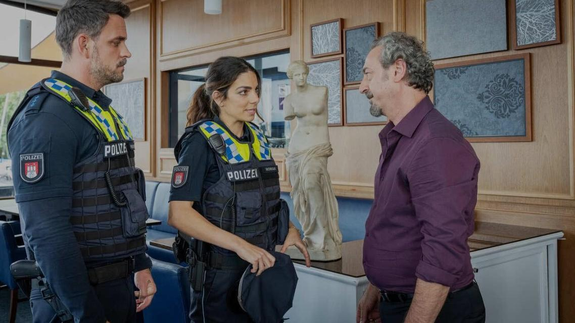 Zwei Polizisten in Uniform sprechen mit einem Mann in einem lila Hemd.