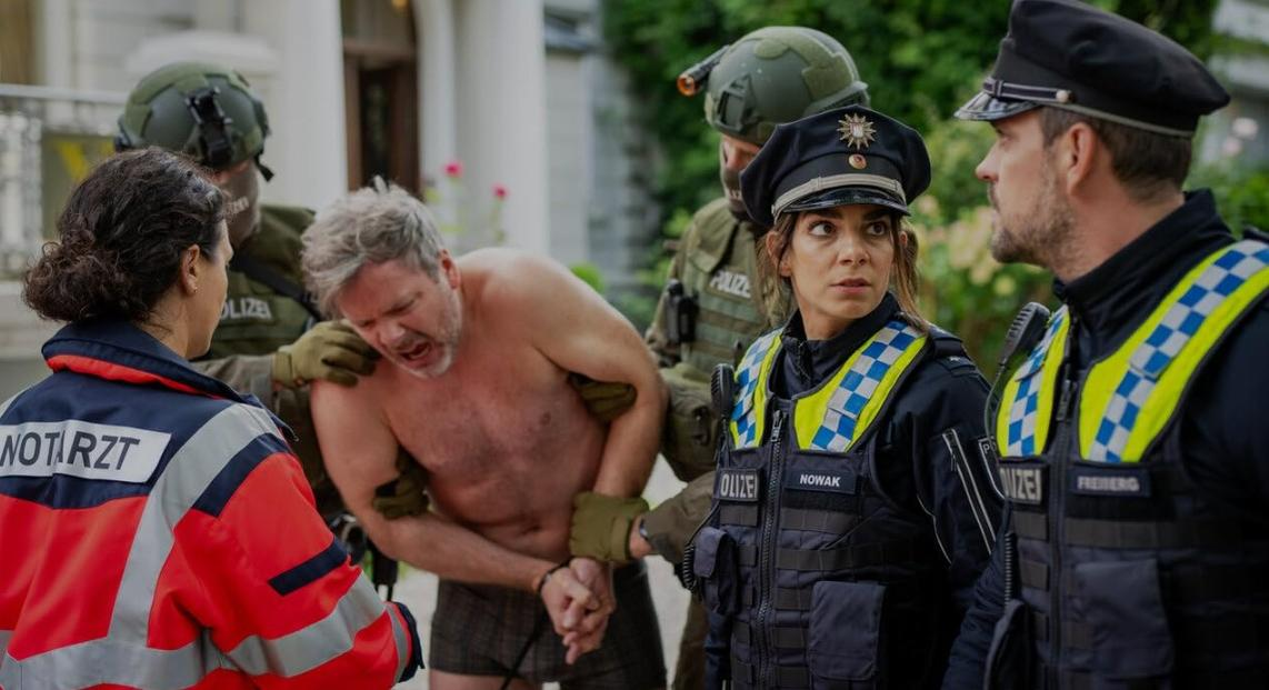Nackter Mann wird von Polizisten und Sanitätern festgenommen. Mann schreit.