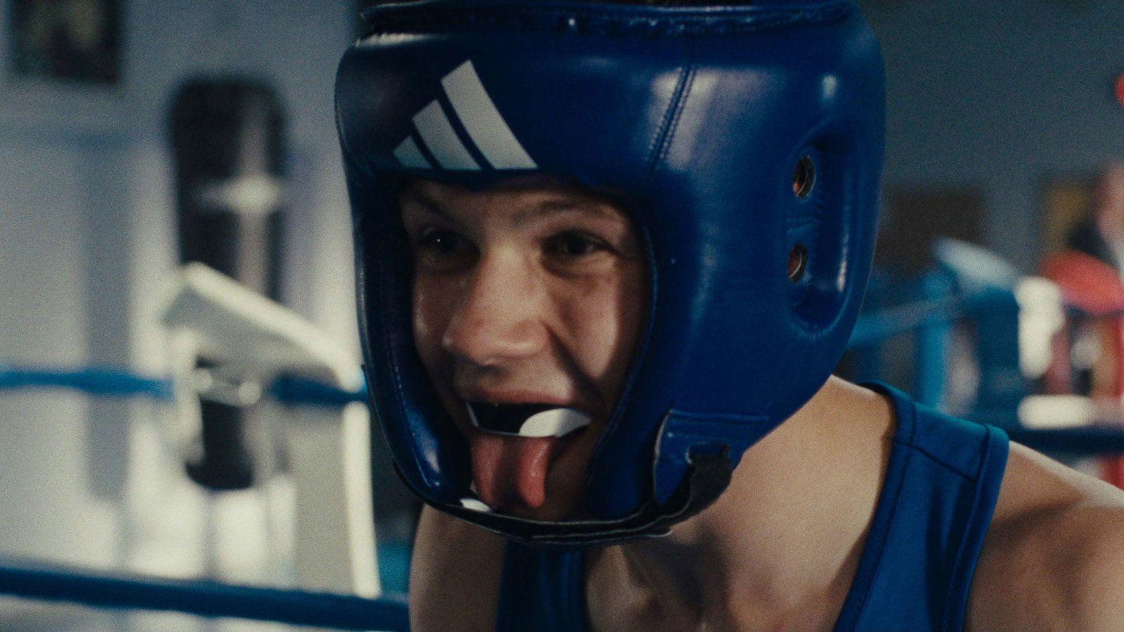 Ein Boxer in einem blauen Kopfschutz mit Mundschutz, der die Zunge herausstreckt.