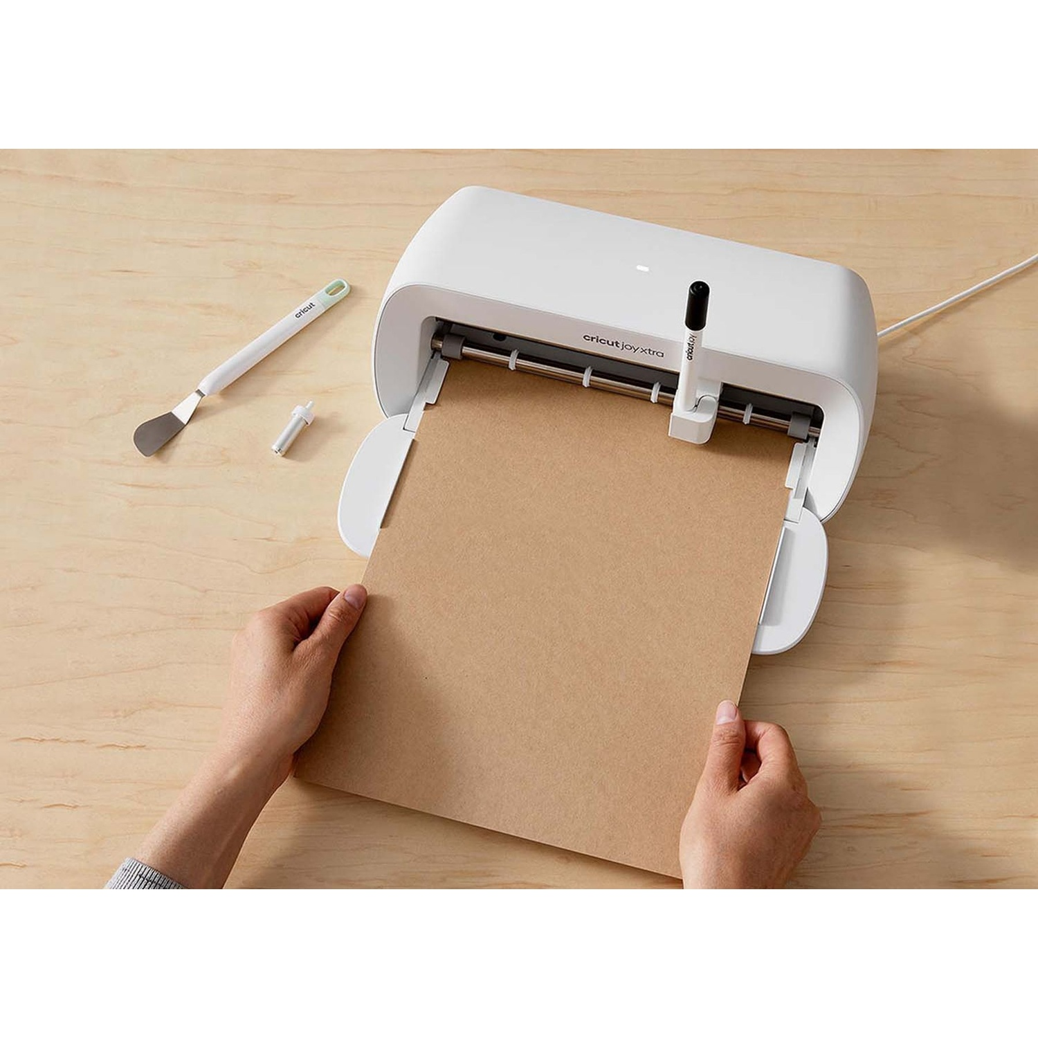 Una persona inserisce carta marrone in una macchina da taglio Cricut Joy Xtra bianca.