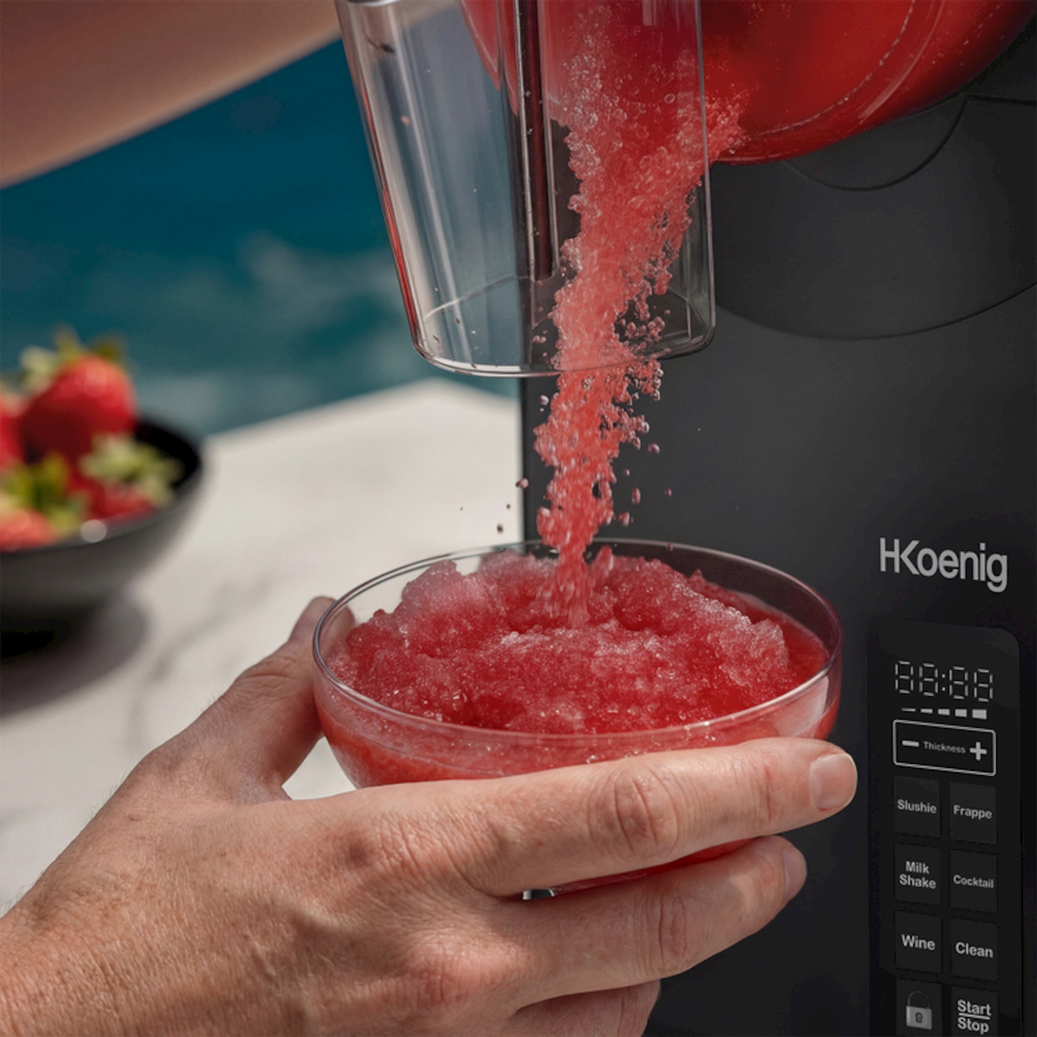 Una persona versa granita rossa da una macchina in una ciotola di vetro. Si vedono fragole.