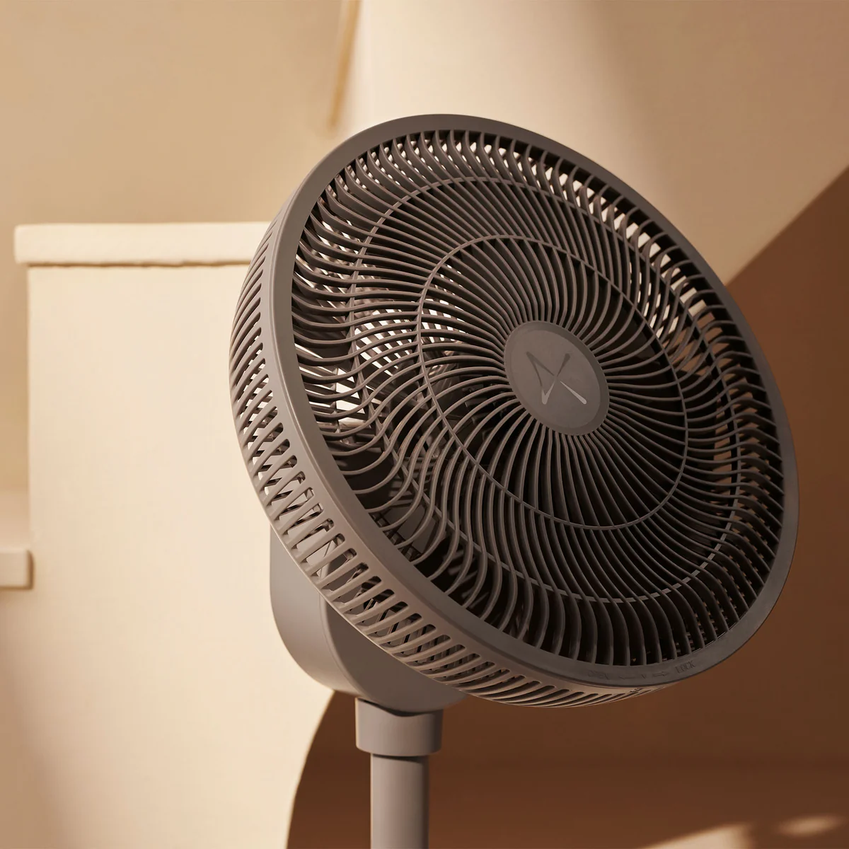Ein grauer Standventilator steht vor einem beigefarbenen Hintergrund mit Schatten.