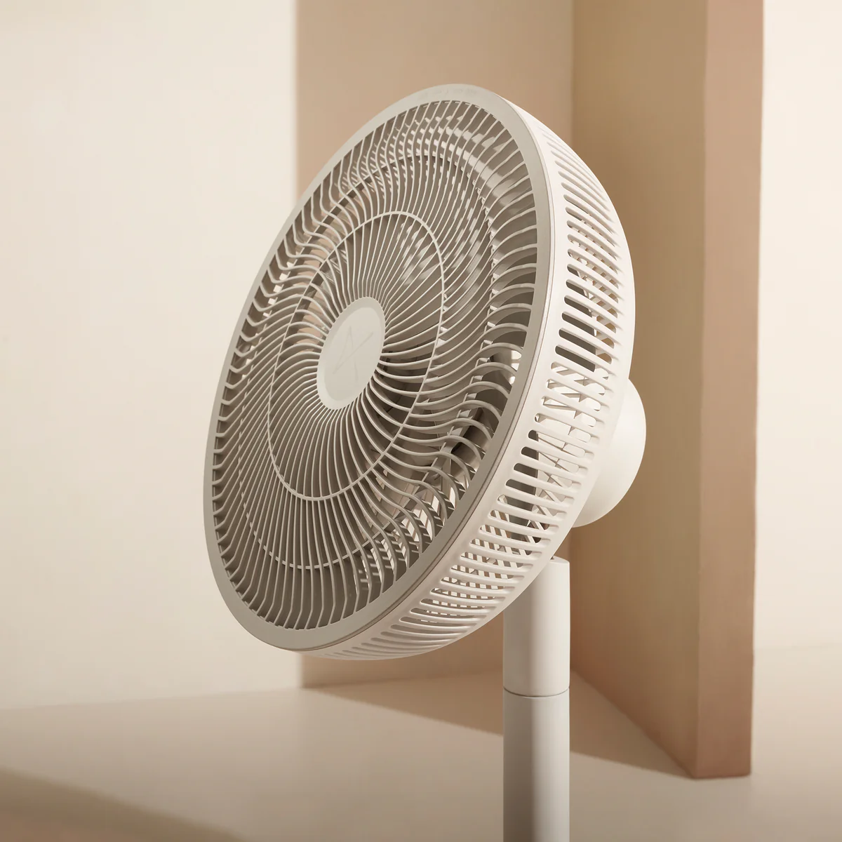 Ein weißer Standventilator mit rundem Gitter und Säule vor einem hellbraunen Hintergrund.