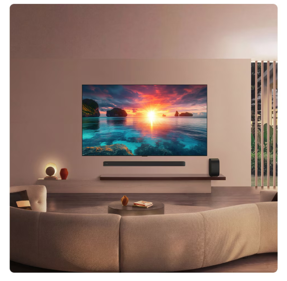 Okyanus üzerinde gün batımını gösteren büyük TV'li modern oturma odası. Kanepe, sehpa, sesli çubuk.