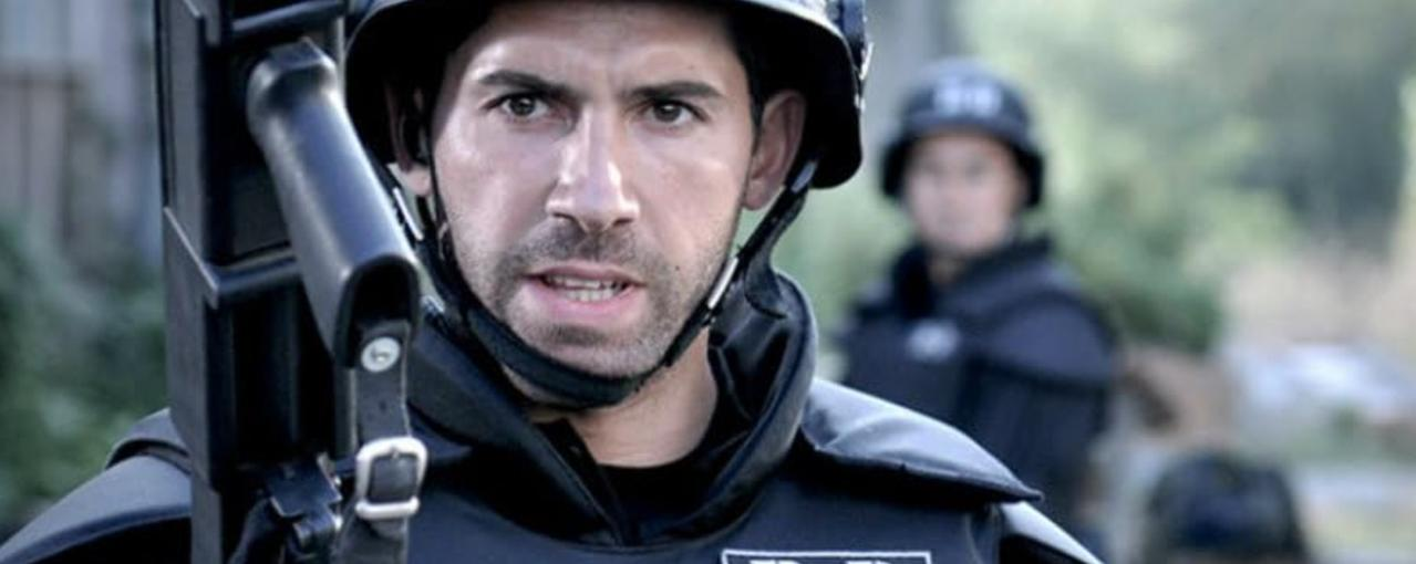 Ein Mann in Schutzausrüstung und Helm blickt angespannt. Im Hintergrund ein weiterer Mann.