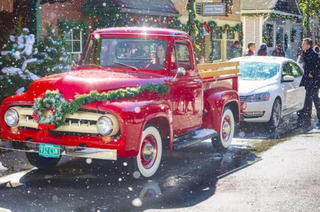 Roter Oldtimer-LKW mit Weihnachtskranz und Girlande, verschneite Straße.